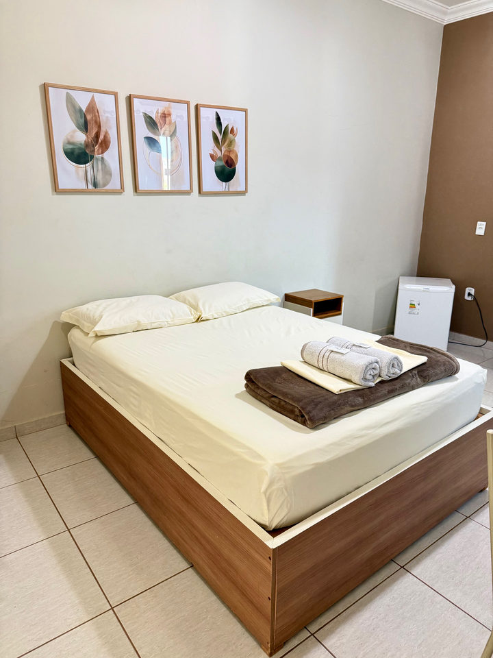 Cama de casal com três quadros botânicos, criado-mudo e frigobar