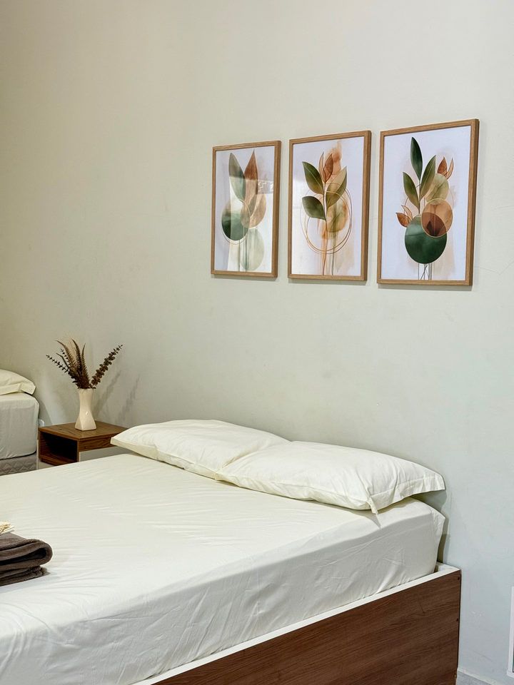 Cama de casal com três quadros e vaso decorativo no criado-mudo