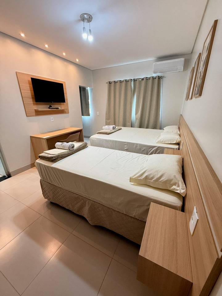 Cama queen e cama de solteiro, com televisão no painel de madeira