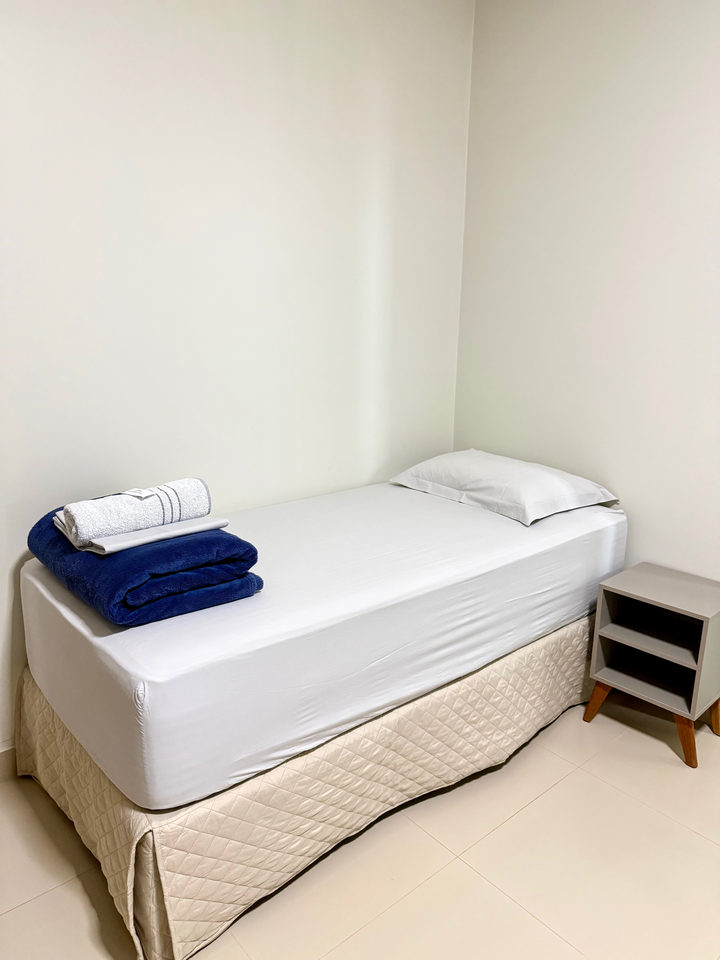 Cama de solteiro com toalhas azuis e criado-mudo ao lado