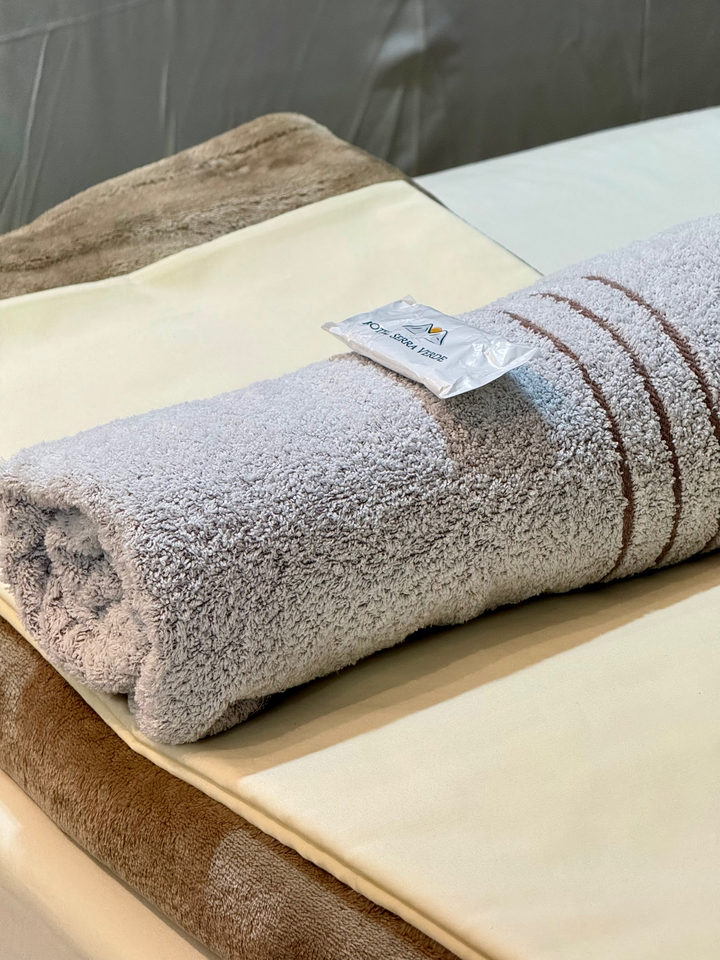 Toalha cinza enrolada sobre o enxoval da cama