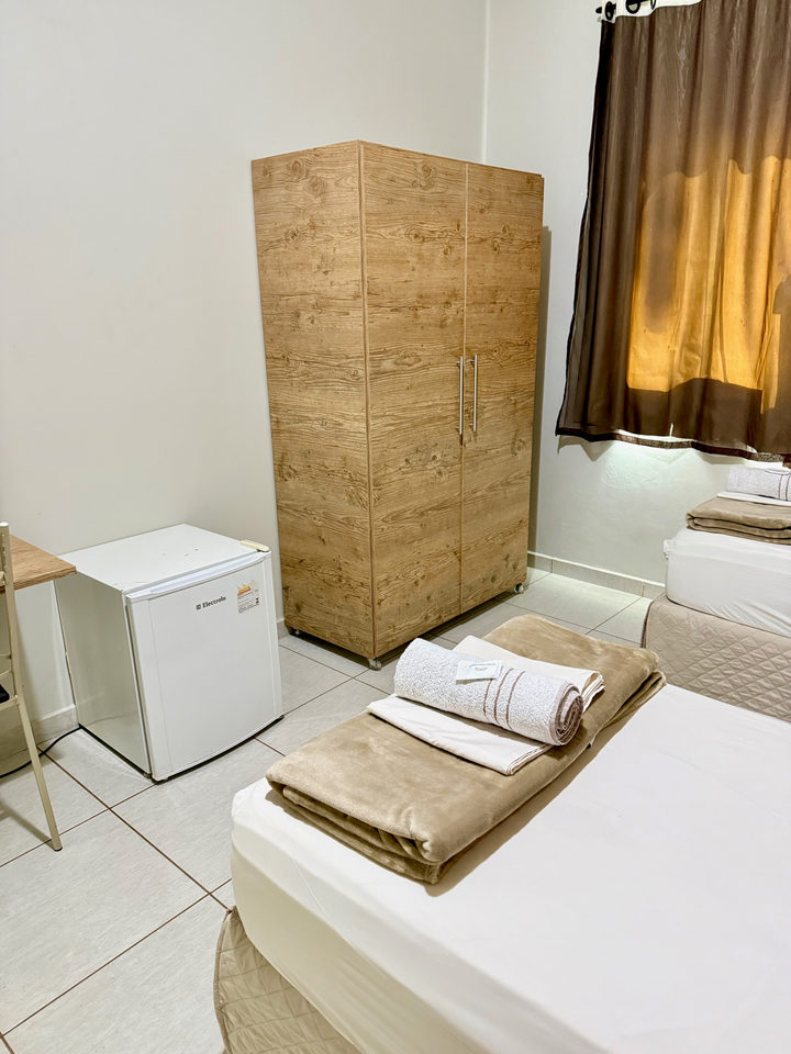 Guarda-roupa de madeira, frigobar e cama com toalhas dobradas